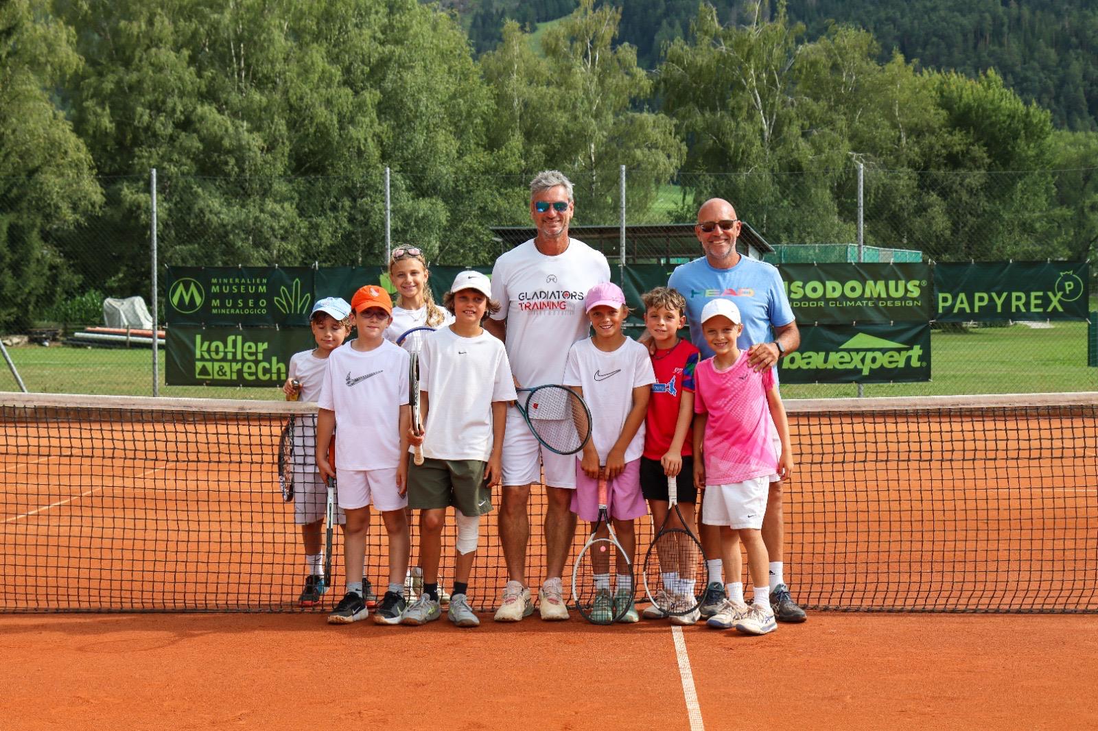 Das Team von Gladiators Training mit einer Gruppe junger Tennisspieler am Spielfeldrand